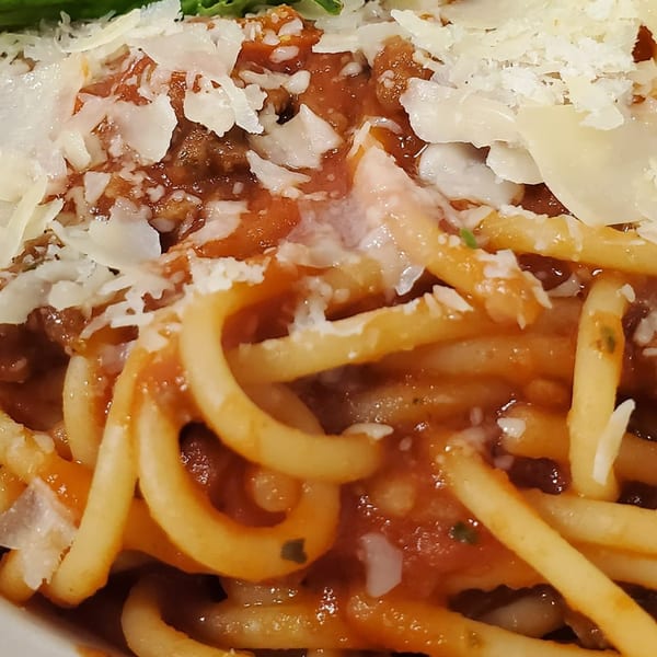 Close-up of spaghetti with red meat sauce and generous shavings of Parmesan cheese.