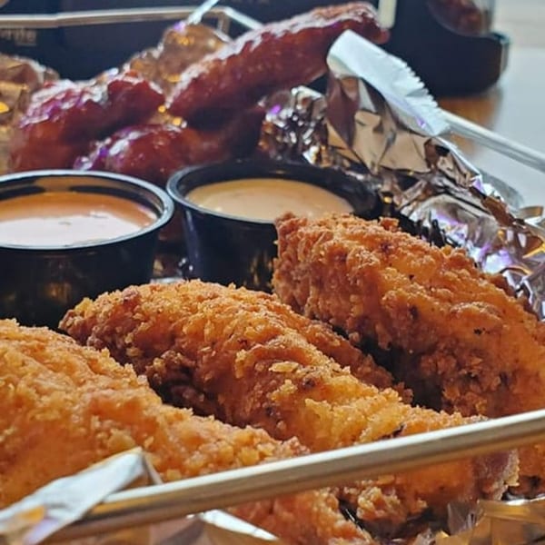 Crispy chicken tenders and saucy wings with dipping sauces in a metal basket.
