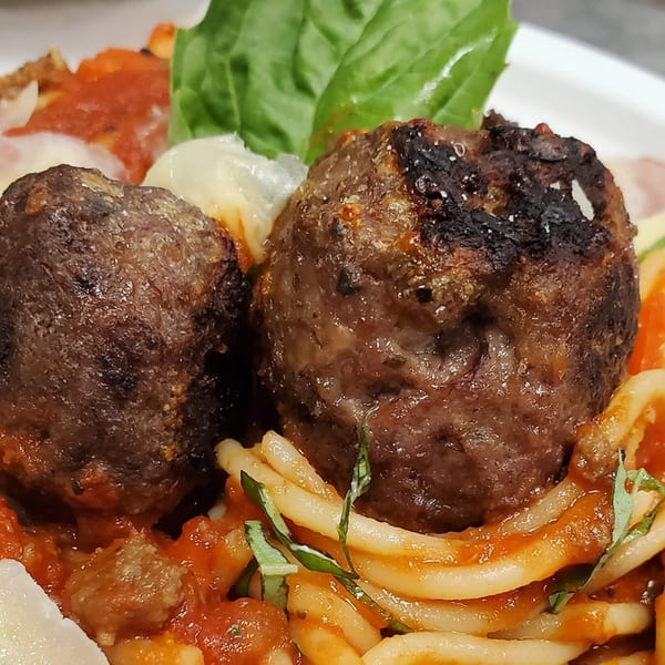 Close-up of two meatballs with pasta, red sauce, and basil on a white plate.
