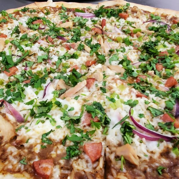 Close-up of a Slice On Oak pizza topped with chicken, red onions, tomatoes, and cilantro.