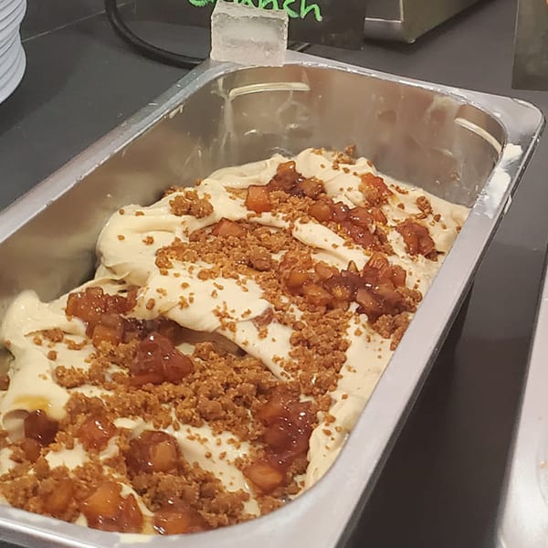 A metal tray filled with creamy gelato, topped with crumbled cookies and apple chunks.