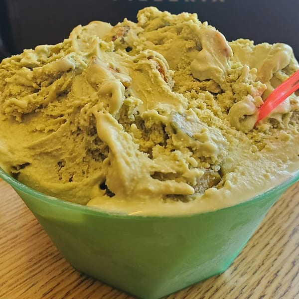 A green bowl overflowing with pistachio gelato, featuring a red spoon, on a wooden table.